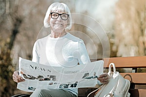 Beaming elegant elderly missis holding paper in the park