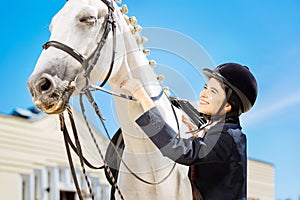 Beaming female rider taking care of her brown racehorse