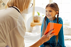 Beaming girl looking at tablet hold by a physician