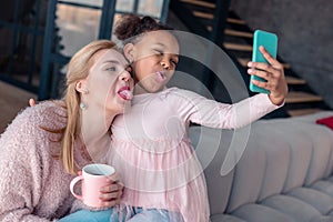 Beaming girl wearing pink blouse making selfie with mother