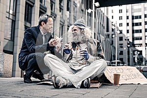 Beaming good-looking man having pleasant conversation with dirty homeless