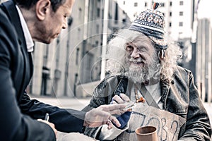 Beaming impressed grey-haired poor man thankfully receiving money
