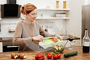 Beaming light-haired woman staying in kitchen and preparing light meal