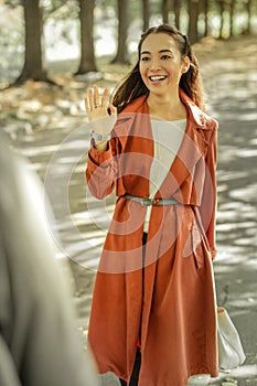 Beaming long-haired girl in red coat waving her hand