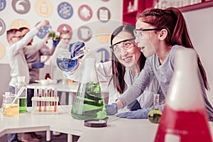 Beaming long-haired teacher mixing liquids in big bulb