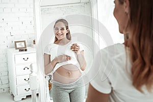 Beaming long-haired woman with wide smile raising white t-shirt