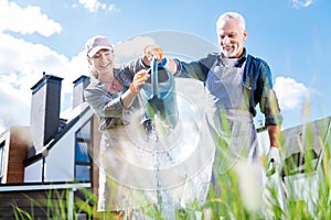 Beaming loving couple holding big garden sprinkler while watering plants