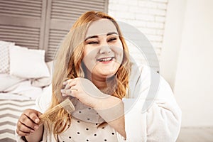 Beaming overweight lady with dismissed hair sitting in bedroom