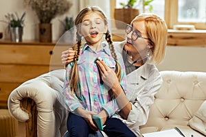 Beaming pediatrician examining lungs of ill girl with a stethoscope