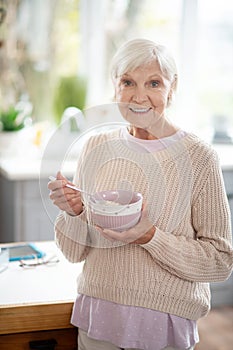 Beaming retired woman smiling while eating oatmeal