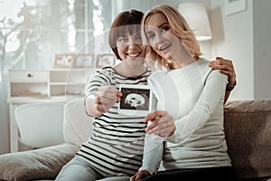 Beaming same sex couple showing ultrasound photo