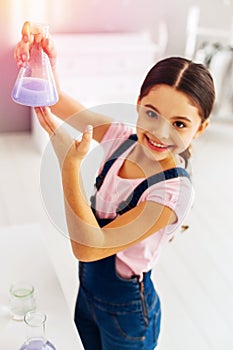 Beaming schoolgirl fond of chemistry holding test tube with blue substance