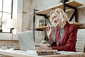 Beaming short-haired blonde businesswoman in red jacket having online call