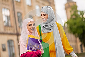 Beaming student holding English book standing near friend