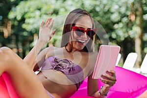 Beaming woman having video chat while swimming in the pool