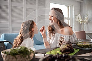 Beaming woman laughing while feeding her cute daughter