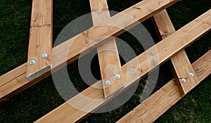 Beams connected by screws in the shape of v. future roof of the pergola fixed to the ground by means of metal foundation profiles