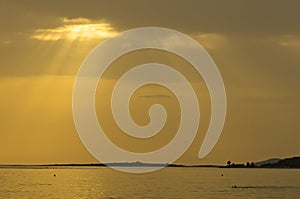 Beams of yellow light with refletions on a water surface before sunset, Sithonia