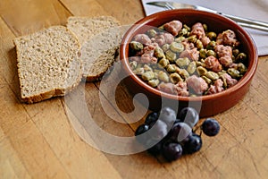 Bean appetizer with onion and sausage presented in a clay plate on a wooden board. Traditional Spanish food. Space for text