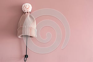 beanie with pompom on a matte black hook, soft pink wall in the background