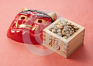 Beans for bean-throwing and masks of ogres placed on a background of red Japanese paper. Japanese ogres