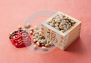 Beans for bean-throwing and masks of ogres placed on a background of red Japanese paper. Japanese ogres