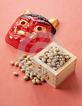 Beans for bean-throwing and masks of ogres placed on a background of red Japanese paper. Japanese ogres