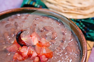 Beans cooked in a clay dish with tomato and tortillas, mexican poor dish