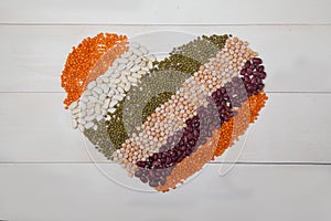 Beans, lentils and beans laid out in the form of a heart on a white wooden background