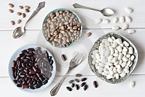 Beans, three types of beans in plates on a background of a white wooden table, vintage spoons and fork