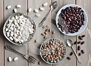 Beans, three types of beans in plates on a background of a white wooden table, vintage spoons and fork