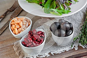 Beans are white and red with large black olives in white small cups with green leaves of arugula and Lollo Ross prepared photo
