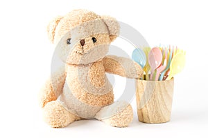 Bear doll sitting with colorful plastic spoon in wooden glass is .