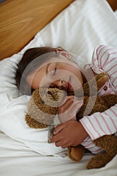 Bear is my bedtime pal. a cute little girl holding her teddybear while sleeping in bed.