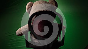 The bear sits and whirls on a chair against the green background of his leg