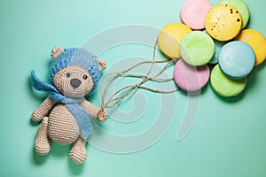 Bear toy holding bunch of colorful macaroons on blue background