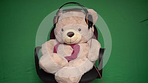 Bear toy teddy in headphones listens to music and nods his head at a green background