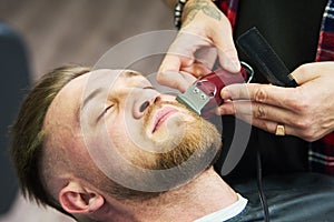 Beard care. man while trimming his facial hair cut at the barbershop