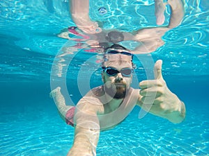 Beard man with glasses diving in a blue clean water with thumb u