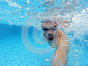 Beard man with glasses swimming under water in the pool