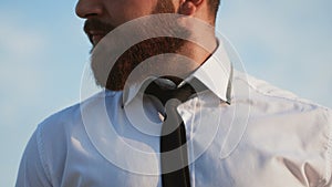 Beard man in white shirt tying the necktie outdoors