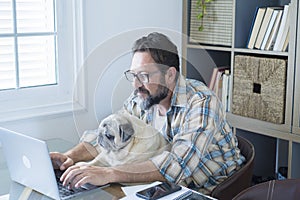 Bearded adult man work at home in office room with his friend dog - people and modern job lifestyle with internet connection and