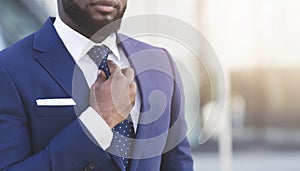 Bearded Afro Businessman Adjusting Tie In Urban Area, Cropped