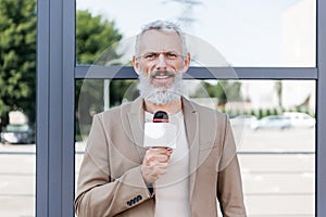 bearded announcer in blazer holding microphone