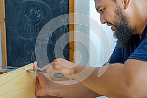 Bearded Asian carpenter using hand saw cutting wooden boards