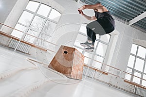 Bearded athlete male jumping over wooden box in sport gym