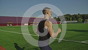 A bearded athlete runs along a running track near green football field, slow motion shooting