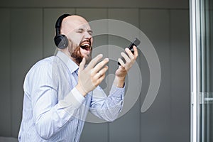 A bearded bald man sings songs and listens to music with headphones at home
