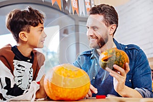 Bearded beaming father feeling memorable carving pumpkins with his son