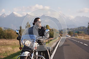 Bearded biker in black leather jacket on modern motorcycle on country roadside.